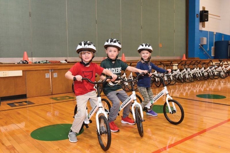 From left: Greenfield Elementary students Ross, Ryan, and Piper try out  new Strider balance bicycles donated to the school by Saratoga Shredders. Photo by Super Source Media Studios. 